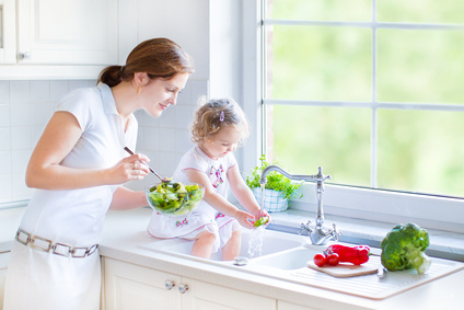 Young mother and her cury toddler daughter washing vegetables